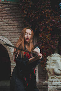 Young woman with statue against brick wall