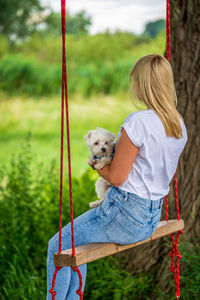 Young woman with a white dog on a tree swing.