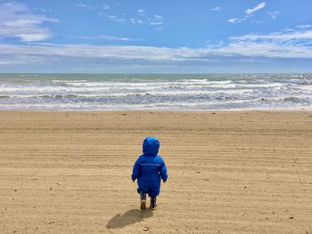 Rear view of boy on beach against sky