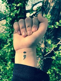 Cropped hand of woman showing tattoo on wrist against tree