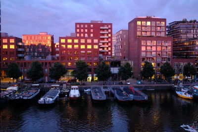 River by illuminated buildings against sky at dusk
