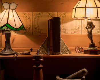 Close-up of illuminated electric lamps and old books on sideboard at home