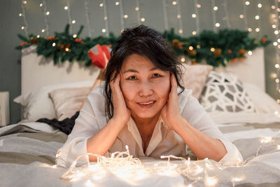 Senior woman relax on bed with xmas lights, charming lady in bedroom at christmas, atmospheric mood