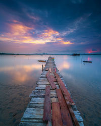 Pier over lake against sky at sunset