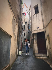 Man walking on narrow alley amidst buildings in city