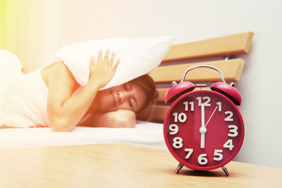 Close-up of alarm clock on table with woman sleeping on bed at home