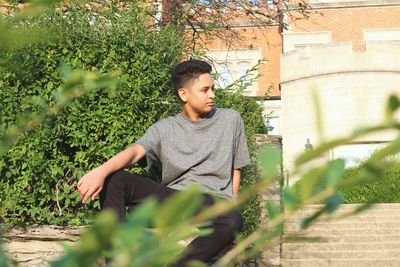 Boy sitting on plant against trees