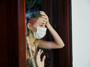 Young woman wearing mask looking away by window