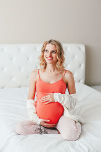 Smiling pregnant woman sitting on bed at home