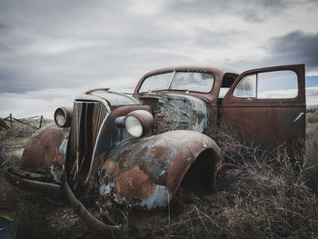 Abandoned car on grassy field against cloudy sky