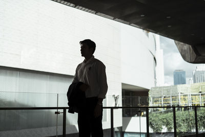 Rear view of man standing by railing against building