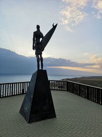 Man standing on railing by sea against sky