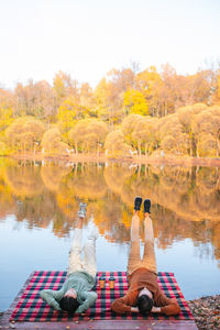 Rear view of people sitting by lake during autumn