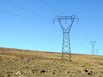 Low angle view of electricity pylons on field against clear blue sky
