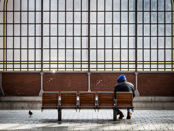 Rear view full length of man sitting on bench at railroad station platform