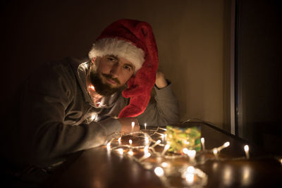 Close-up of young man by illuminated christmas lights on gift in darkroom