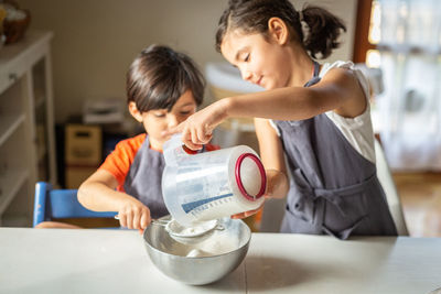 Two sisters wearing grey aprons sifting flour