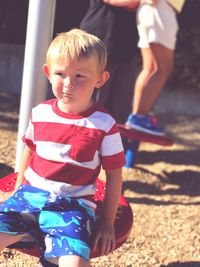 Boy looking away while sitting on seat at playground