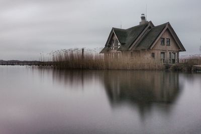 House by lake against sky