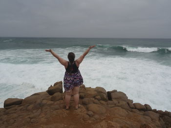 Rear view of woman standing on rock formation against sea