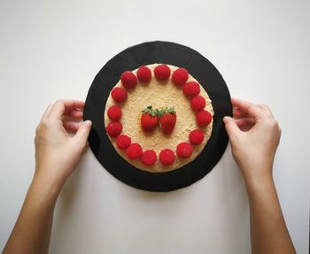Directly above shot of hand holding strawberry over white background