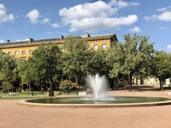 Fountain by trees and buildings against sky