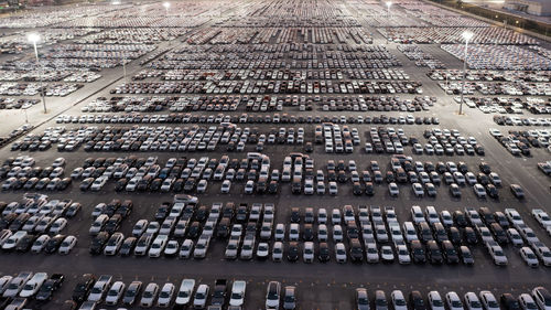 New cars parked at distribution center automobile factory at night with lights. aerial view