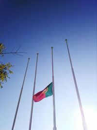 Low angle view of flag poles against clear blue sky