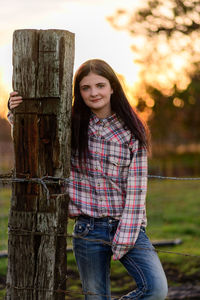 Portrait of young woman standing against fence post