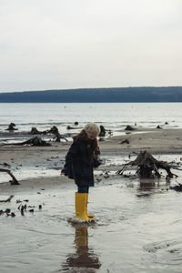 Girl in big yellow rubber boots walking at seashore