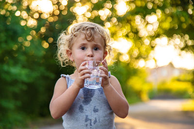 Portrait of young woman drinking water bottle against trees