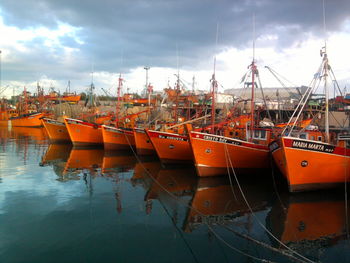 Orange boats moored at harbor against cloudy sky