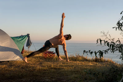 Adult man does physical exercises at sunrise, in front of the te