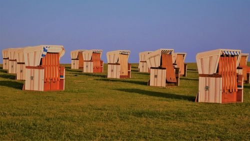 Hooded chairs on field against clear blue sky