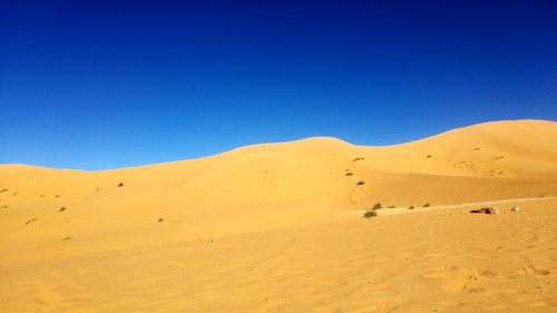 Low angle view of sand dunes against clear blue sky