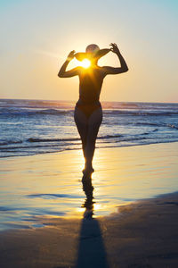 Silhouette woman with arms raised against sea during sunset