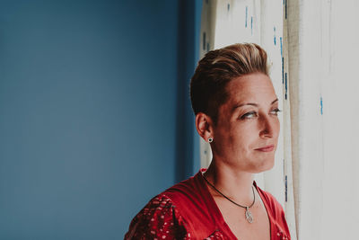 Mature woman looking away while standing by window at home