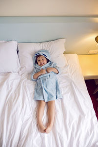 Baby boy two years old in a blue terry robe with a hood lying on a big bed