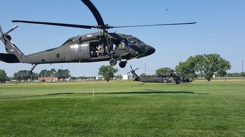 Two black hawk helicopters taking off in a field with soldiers inside 