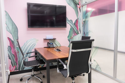 Small wooden conference table with comfortable chairs in creative office with modern tv hanging on wall with floral print