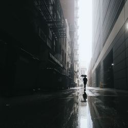 Silhouette man with umbrella walking on wet street amidst buildings in city