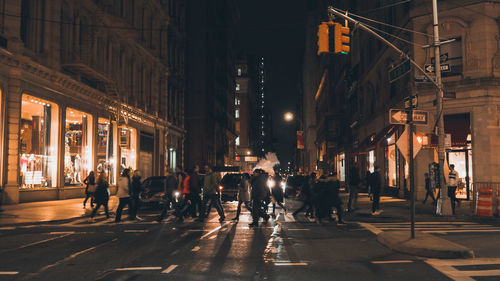 People walking on illuminated street amidst buildings at night