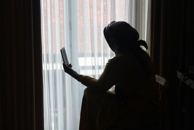 Silhouette man looking through window at home