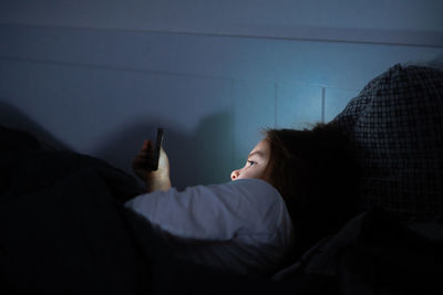 Side view of girl using smart phone lying on bed