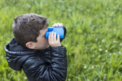 High angle view of boy looking through binoculars while standing on grass