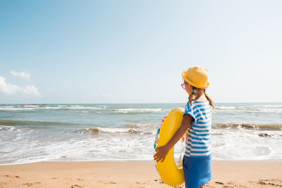 Rear view of woman standing at beach against sky