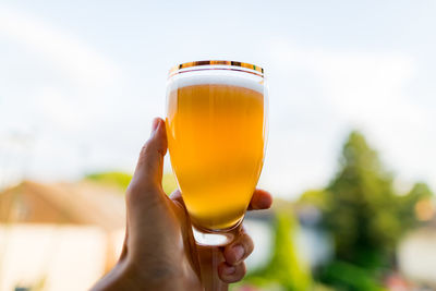 Close-up of hand holding drink against sky