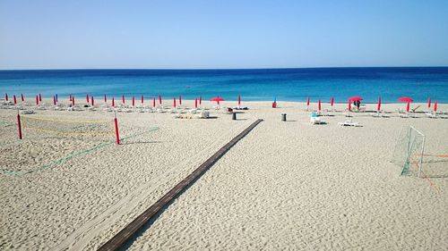 Closed red parasols at beach against clear sky