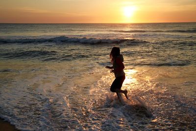 Full length of woman standing at beach during sunset