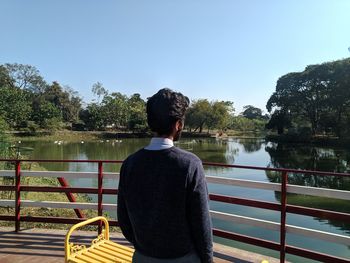 Rear view of man looking at lake against sky